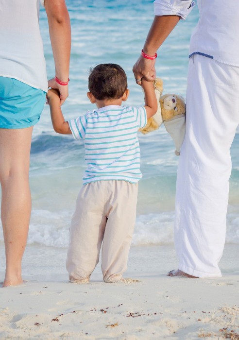 A child on the beach holding hands with parents
